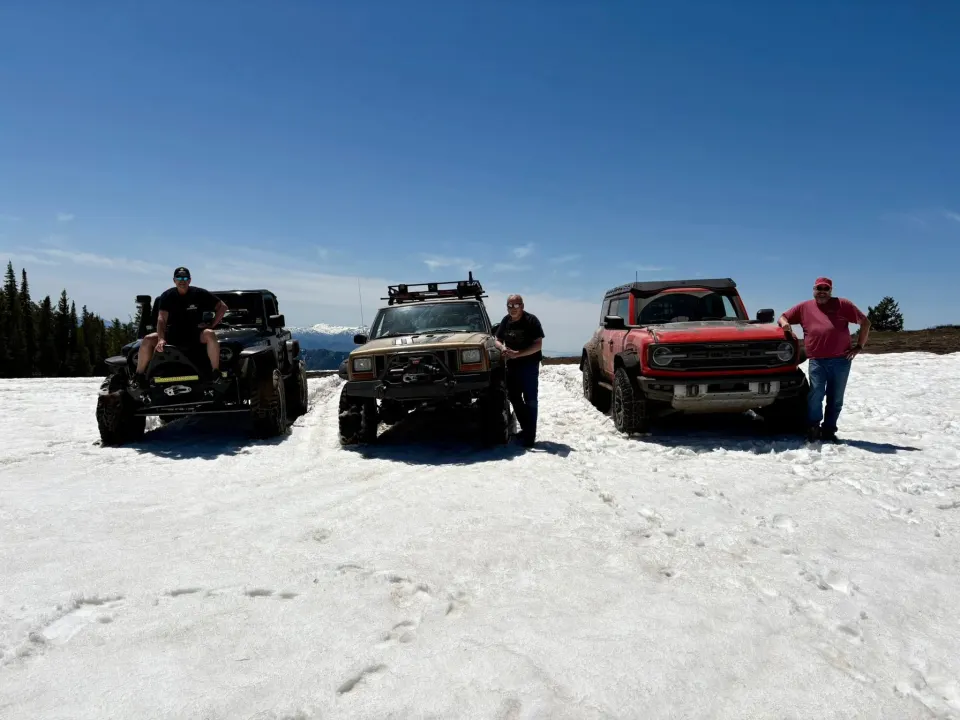 Three club members beside their four-wheel-drive vehicles on a snowy outing